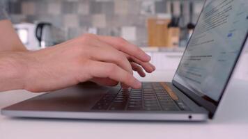 fechar acima do homem mãos digitando em computador portátil teclado. Ação. lado Visão do masculino mãos e dele computador portátil em borrado fundo do uma cozinha, o negócio e comunicação conceito. video