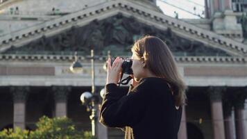 Young beautiful woman taking photos on background of temple. Media. Woman takes photos with professional camera on background of temple. Romantic rays of sun falling on woman photographer video