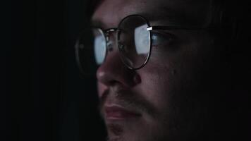 Business man, coder or programmer working late at night with laptop. Concept. Thoughtful focused guy in the dark with the computer screen reflected in his glasses. video