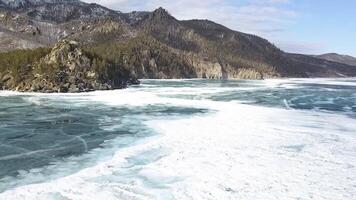 Beautiful views of a frozen winter lake with snowy forested mountains. Clip. Aerial view of frozen water reservoir of turquoise color and coniferous forest on mountain slopes. video