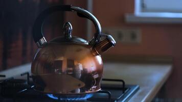 Close up of a stainless steel tea kettle on a flaming gas stove. Concept. Heating kettle with the reflection of the kitchen on its metal surface, preparation of hot beverage. video