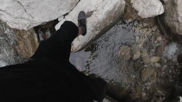 natural paisaje de montañoso río con un hombre saltando desde Roca a Roca. acortar. primero persona disparo de masculino piernas cruce rápido fluido río con grande piedras en el salvaje bosque. video