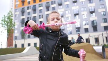 contento bambino giocando all'aperto con sapone bolle su terreno di gioco nel presto autunno. azione. concetto di infanzia e tempo libero, avendo divertimento nel il strada. video