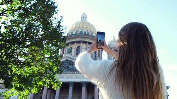 ung kvinna på Semester fotografering med henne smart telefon en skön historisk byggnad. begrepp. bak- se av en ung turist stående och använder sig av en smartphone till ta foton av en katedral under video