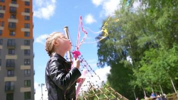 pequeño hermosa niña creando jabón burbujas mientras gasto hora en el ciudad parque cerca verde arboles acción. concepto de infancia y divertido, contento niño jugando al aire libre. video