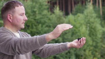 Caucasian man with a big butterfly of black and yellow colors in his hand. Video. Side view of a middle aged man touching a tropical butterfly on the background of green forest. video