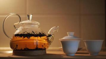 Teapot with fresh tea leaves in hot water and small cups on the kitchen table. Concept. Close up of glass transparent teapot with brewing black tea, concept of tea ceremony. video