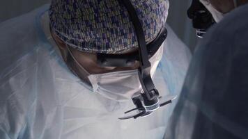 Doctors in masks and special glasses performing operation. Action. Close-up of focused faces of surgeons performing complex operation under anesthesia. Specialized surgical equipment video