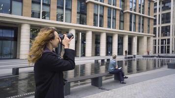 mujer toma imágenes de banco edificio. acción. mujer fotógrafo camina alrededor ciudad y toma imágenes de moderno arquitectura de negocio centros video