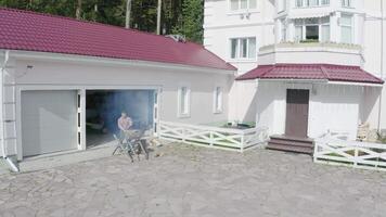 Man saws log in yard for fireplace. Video. Top view of man sawing log in yard on background of garage of country cottage. Luxury vacation in country video