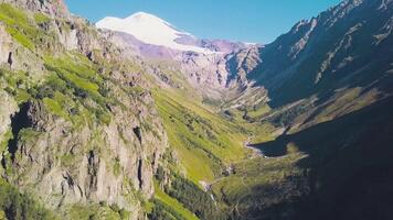 Top view of mountain landscape with snowy peak and green slopes. Clip. Majestic rocky mountains with green forest and snow-capped peaks. Spectacular mountain landscape on sunny day video