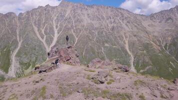 Climbers stopped to rest in mountains. Clip. Tourists on ascent to mountains stopped to rest on rocky ledge. Mountaineers relax in mountains on background of mountains that take your breath away video