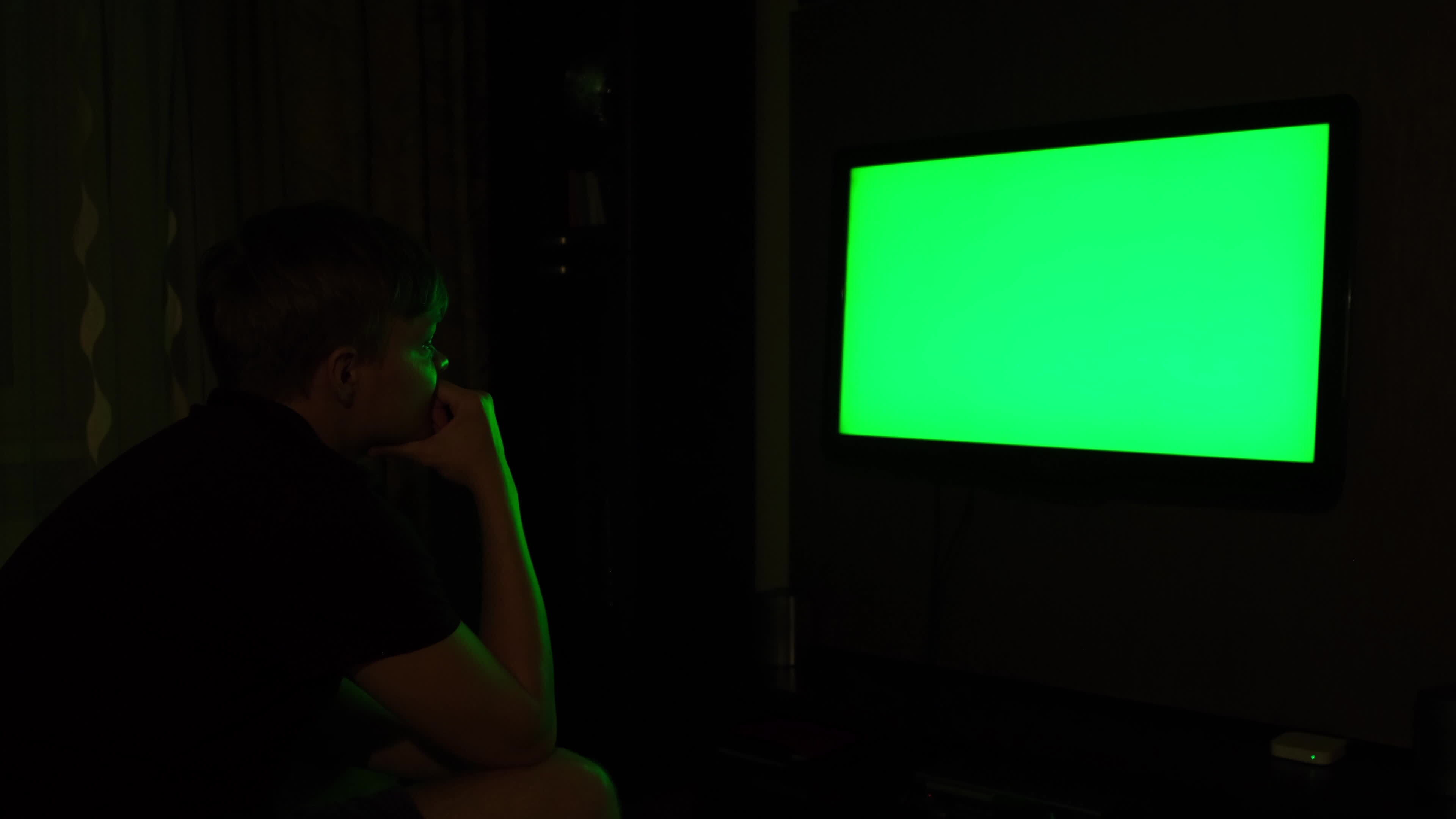 Side view of a young man watching TV with chromakey while sitting on a