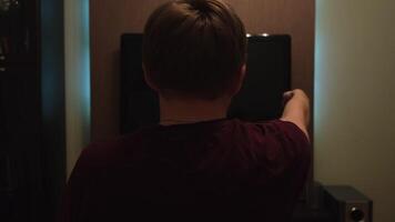 Young man turning on TV and watching football game at home. Concept. Rear view of a man sitting on a couch at home and watching football late in the evening. video