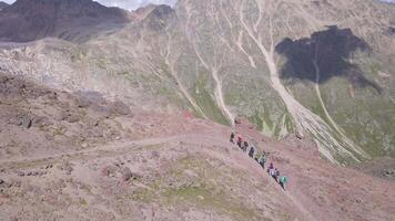 aereo Visualizza di escursioni a piedi squadra a piedi uno di uno, arrampicata su il montagna pendenza. clip. viaggio e sport stile di vita concetto, gruppo di turisti a piedi in direzione il montagna vertice. video