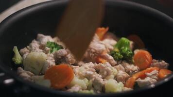 Cooking a chicken with vegtables in a frying pan. Concept. Close up of stirring and simmering vegetables and meat with a wooden food turner, healthy diet. video