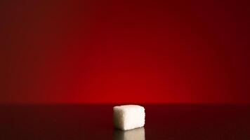 singolo cubo di zucchero isolato su rosso sfondo. azione filmato. vicino su di un' bianca zucchero cubo in piedi nel il ombra con luminosa leggero splendente Poi. video
