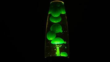 Green lava lamp on black background. Concept. Beautiful neon-lit lava lamp in total darkness. Retro neon night light with moving bubbles. Lava lamp video