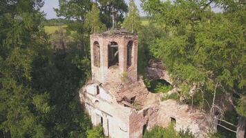Abandoned church in the forest. Clip. Aerial view of the old church with a bell tower and a ruined dome on the background of green trees in bright sunny colors. video