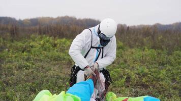 hombre lleva paracaídas. acción. hombre lleva multicolor paracaídas después aterrizaje. hombre en mono arrastra paracaídas a reunión sitio en campo. extremo deporte y paracaidismo video