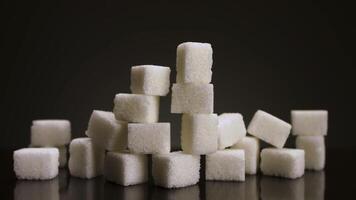 Close up of growing pile of sugar cubes isolated on dark grey background. Stock footage. Stop motion effect, concept of the sugar increasing consumption. video