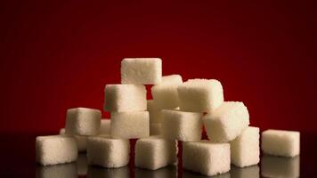 Close up of growing pile of sugar cubes isolated on dark red background. Stock footage. Stop motion effect, concept of the sugar increasing consumption. video