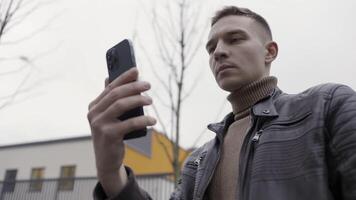 Bottom view of a man holding new beautiful smartphone in his hands. Action. Young man taking a panoramic picture or making a video on cloudy grey sky background.