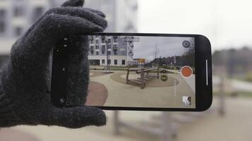 dichtbij omhoog van technologie demonstratie van een smartphone camera gedurende video het schieten van een kinderen speelplaats. actie. vinger drukken Aan scherm en kiezen zoomen modus, normaal modus, en breed hoek