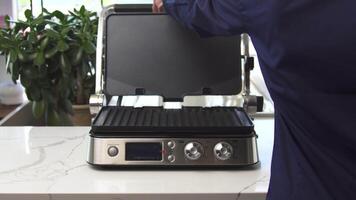 Hem använda sig av elektrisk grill på polerad vit tabell på de affär av Hem apparater. hushåll redskap. manlig händer öppnas tömma modern elektrisk grill. video