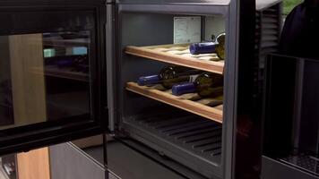 Wine bottles cooling on refrigerator wooden shelves. Household utensils. Close up of home use wine cooler, man opens the door of a cooling machine. video