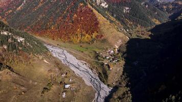 aéreo ver de un encantador pequeño pueblo situado abajo en el Valle cerca boscoso sierras. imágenes. volador terminado el montañas cubierto por vistoso otoño arboles video