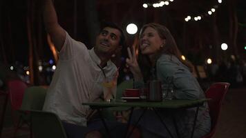 joven Pareja en romántico cena tomando selfie retrato foto con inteligente teléfono. medios de comunicación. contento hombre y mujer gastar hora juntos a el al aire libre terraza de un restaurante a noche en el Hora de verano. video