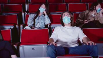 joven gente en médico mascaras riendo a cine teatro. medios de comunicación. alegre alegre audiencia acecho divertido comedia en cine y vistiendo médico mascaras, prevención de codicioso 19 virus. video