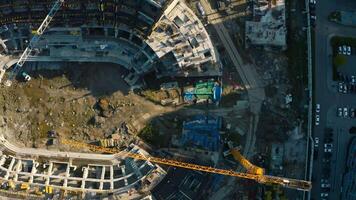 Vertical top view of construction of circular building. Stock footage. Construction site of building near parking lot in city center. Construction of stadium in center of residential city on sunny video