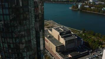 Top view of glass facade of high-rise building with landscape of city and river. Stock footage. Beautiful landscape of modern city with glass buildings. Glass skyscrapers with green landscapes of video