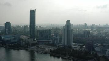 parte superior ver de moderno gris ciudad en nublado clima. valores imágenes. gris nublado ciudad con río y niebla. nublado día colgando terminado moderno ciudad video