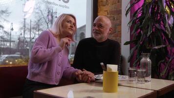 Beautiful elderly couple on date in cafe. Stock footage. Beautiful elderly couple is chatting on date. Stylish elderly couple chatting in cafe video