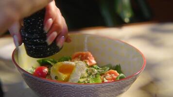 avvicinamento di donna aggiungendo spezie per insalata. azione filmato. donna Pepe insalata con uovo. sostanzioso condito insalata o ciotola con bellissimo servendo video