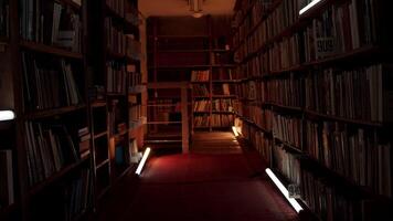 Night library with flashing lights. Stock footage. Corridor with bookshelves in night library. Flashing lights in aisle between bookshelves of night library video