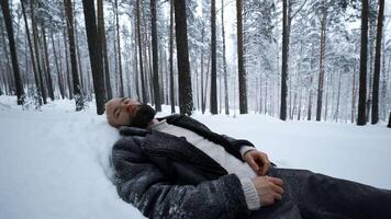 Man lies in snow in winter forest. Media. Tired man lies in snowdrift in winter forest. Depressive Stylish man lies in snow in winter forest video
