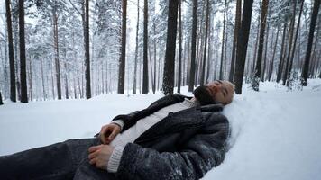 homem mentiras dentro neve dentro inverno floresta. meios de comunicação. cansado homem mentiras dentro monte de neve dentro inverno floresta. depressivo à moda homem mentiras dentro neve dentro inverno floresta video