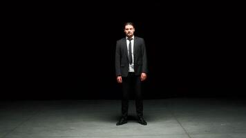 uomo nel completo da uomo sta emotivamente su palcoscenico. azione filmato. uomo nel completo da uomo sta su palcoscenico con drammatico Guarda. elegante drammatico uomo su buio palcoscenico nel emotivo produzione video