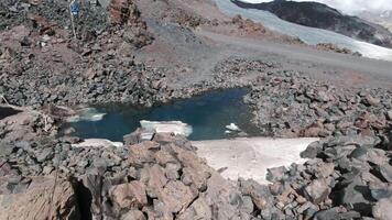 un' pozzanghera di acqua su un' montagna roccia. clip. soleggiato montagna pendenza con un' pozzanghera di buio blu acqua circondato di grande e piccolo pietre. video