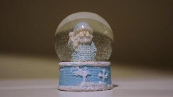 Christmas magic ball with Father Frost. Concept. Close up of a New Year symbol - glass ball with falling snow inside, souvenir standing on white table surface. video