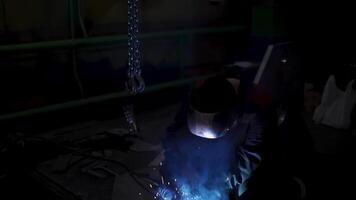 A laborious worker in a uniform and a protection mask during welding process. Clip. Welder in a workshop of a plant working with metal details. video