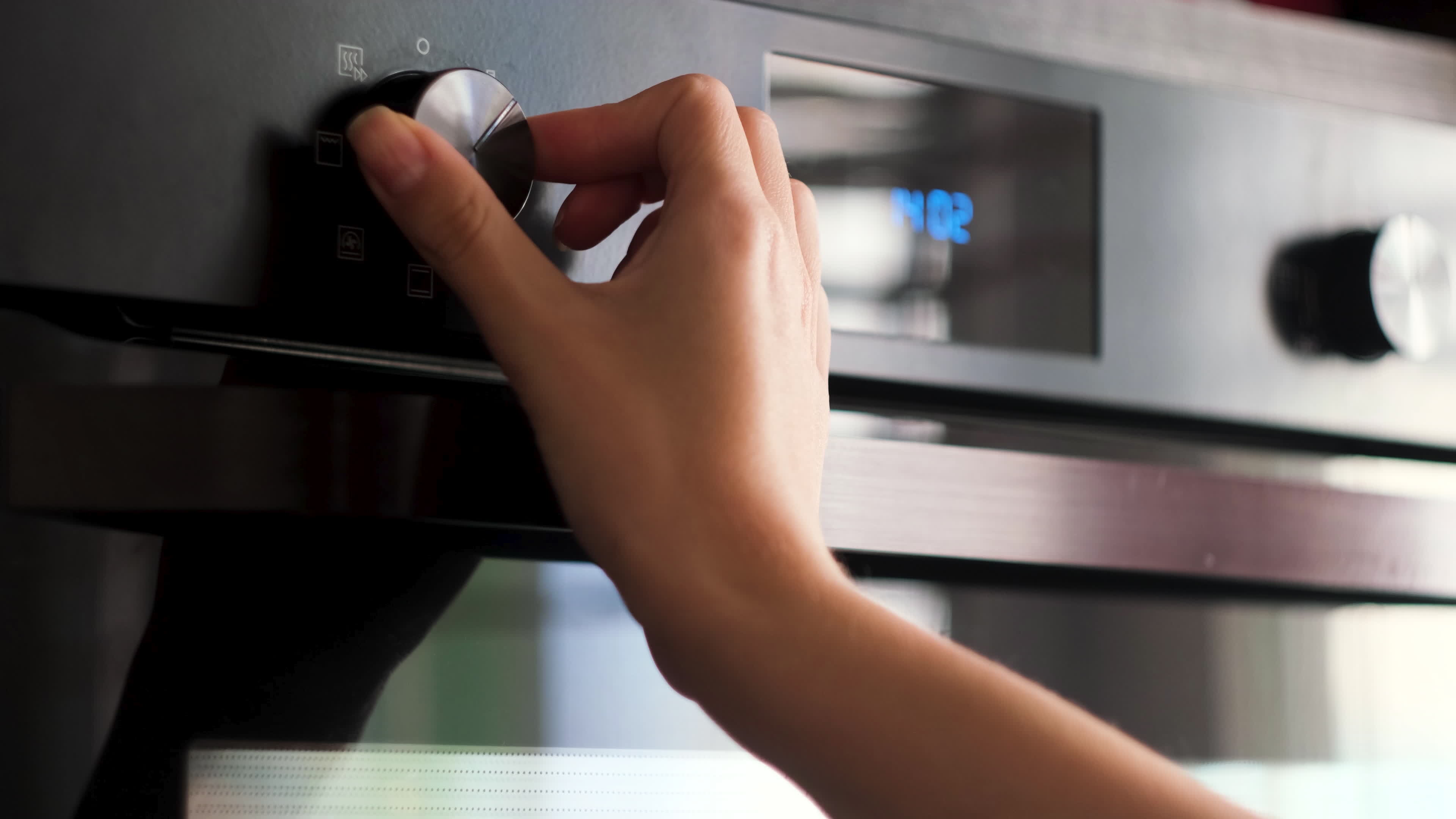 Woman twisting the handle of a modern oven. Concept. Details of cooking