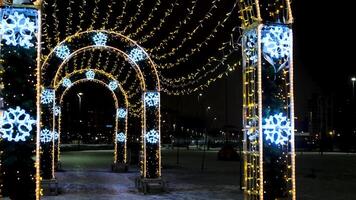 jul illumination och dekorationer i de stad gata i en form av valv. begrepp. skön lampor som en symbol av vinter- högtider, lysande krans på svart himmel bakgrund. video