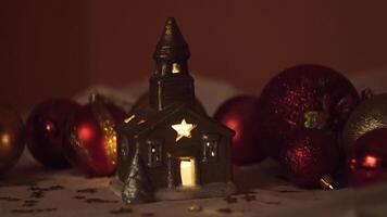 Beautiful little toy house with a candle inside. Concept. Close up of beautiful light of a candle inside a small church toy on red spruce tree balls background. video