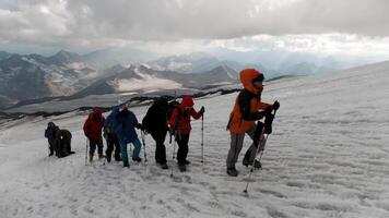 i viaggiatori salire lungo il montagna passaggio su il ghiaccio pendenza. clip. concetto di estremo sport e hobby, scalatori su il sfondo di montagna gamma e pesante nuvole. video