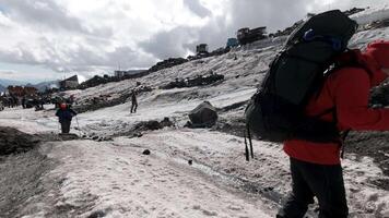 bergsklättrare gående upp en kulle längs en snöig backe nära läger bas. klämma. Västra alperna, Europa utforska värld genom aktiva livsstil. video